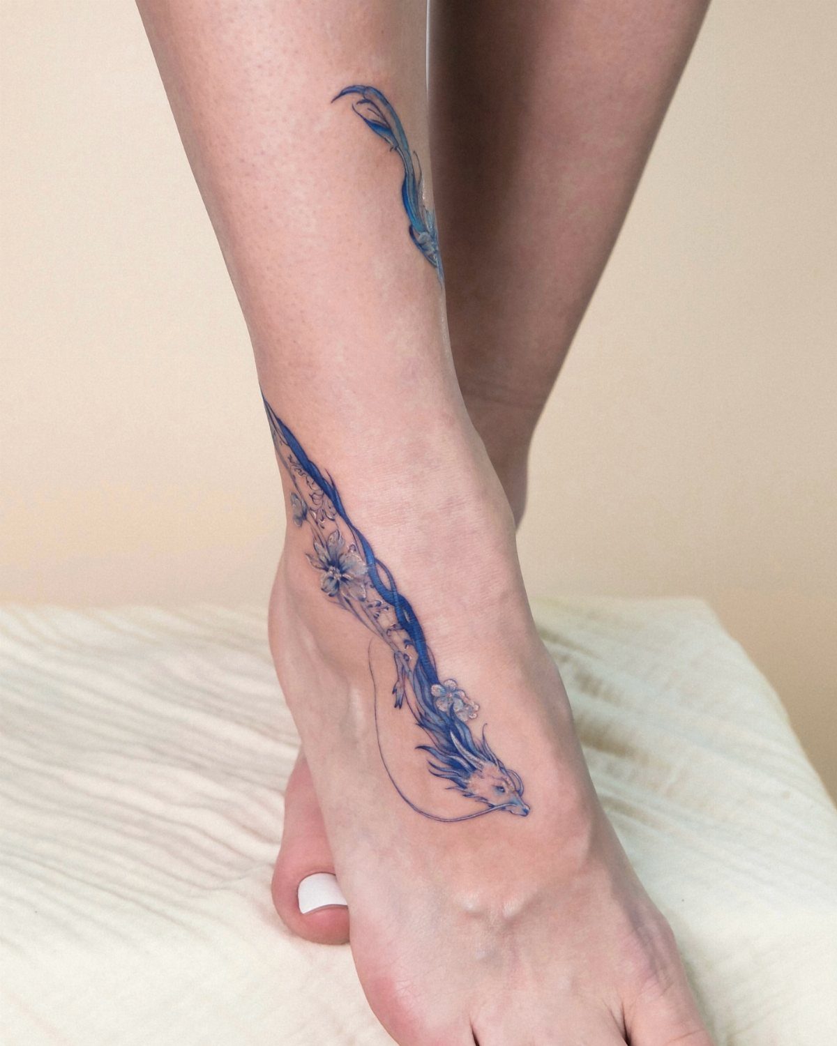Blue abstract dragon tattoo curving around a woman's ankle and foot.