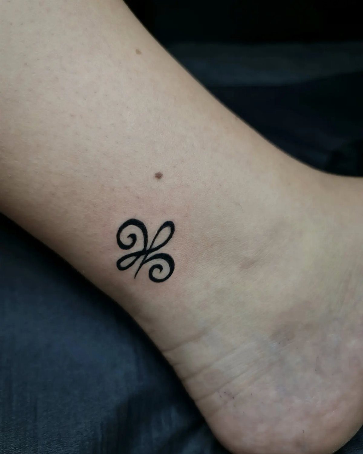 Small black Celtic knot tattoo on the side of a person's ankle.