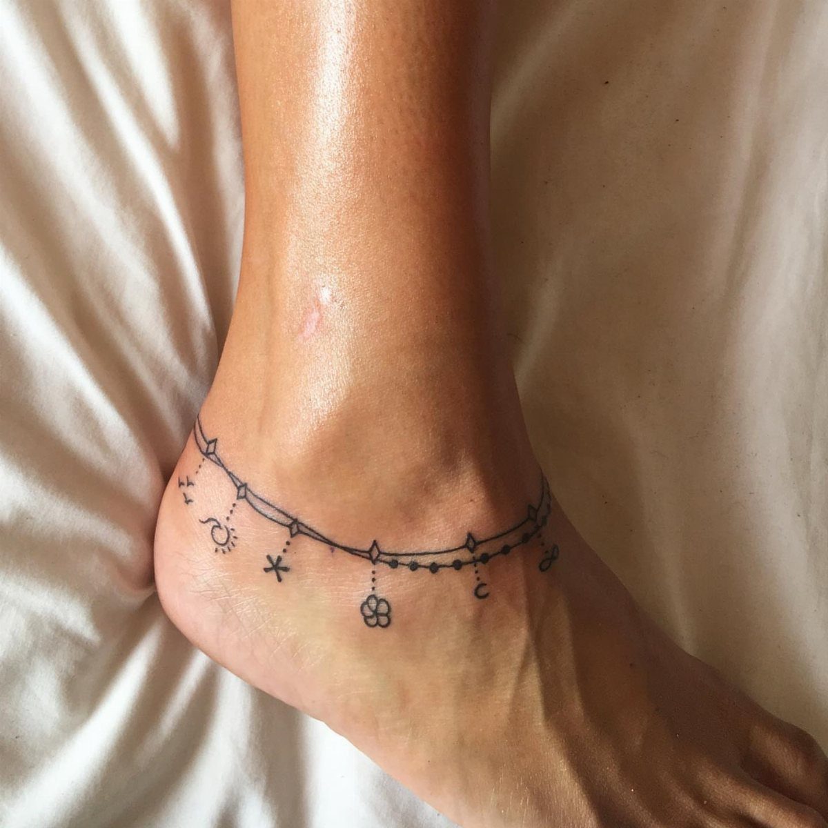 Ankle tattoo designed as a charm anklet with small symbols and a clover.
