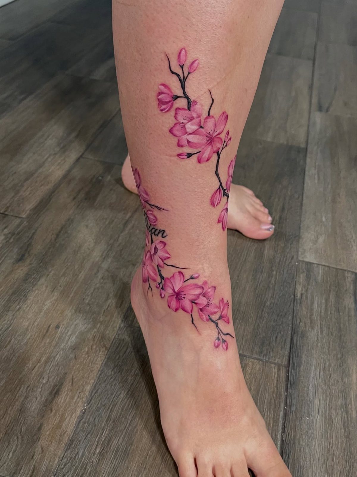 Pink cherry blossom tattoo wrapping around a person's ankle and lower leg.