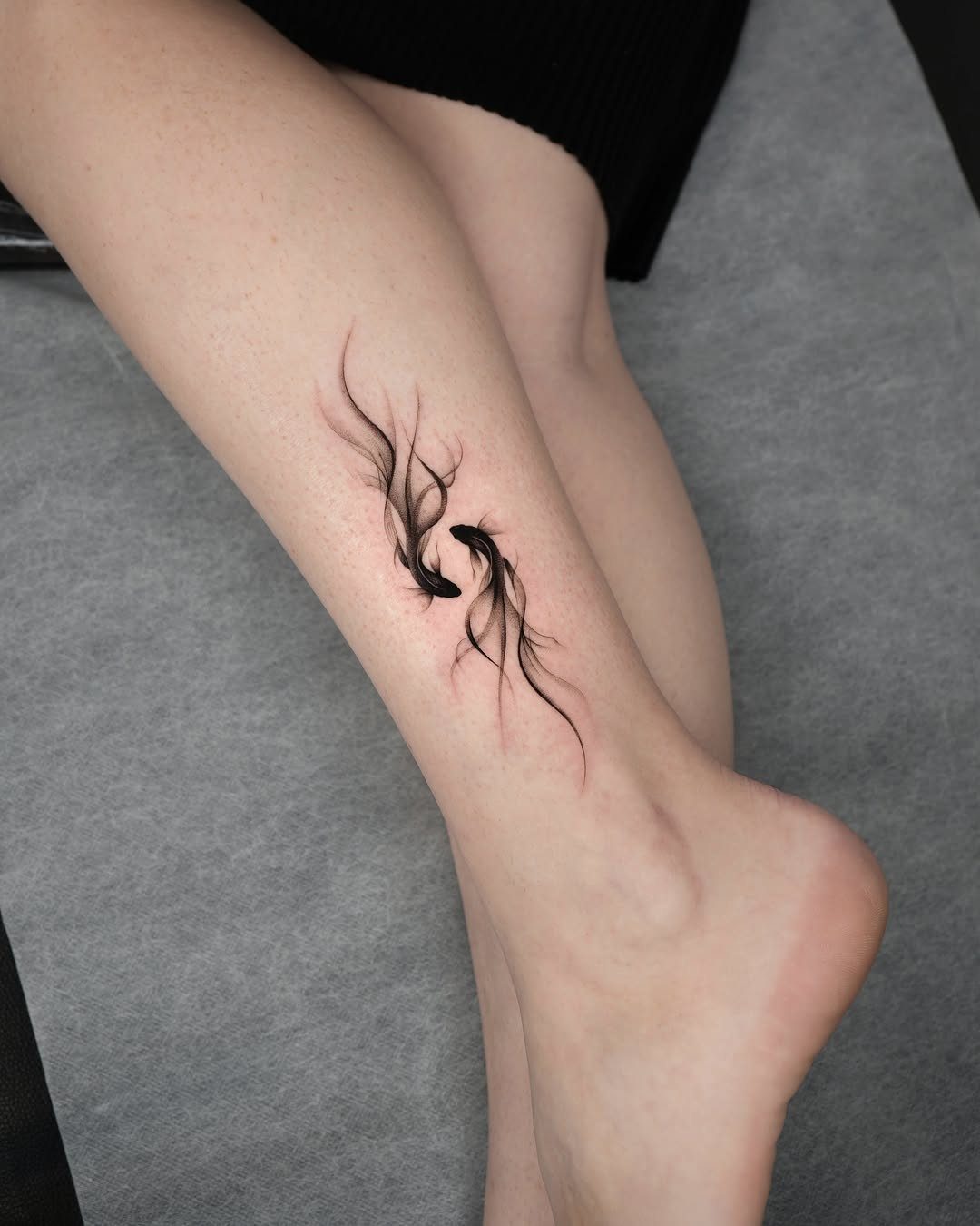 Two black koi fish tattoo with red accents on a person's ankle