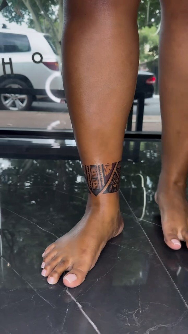 Ankle tattoo with black geometric patterns and lines wrapping around a person's leg.