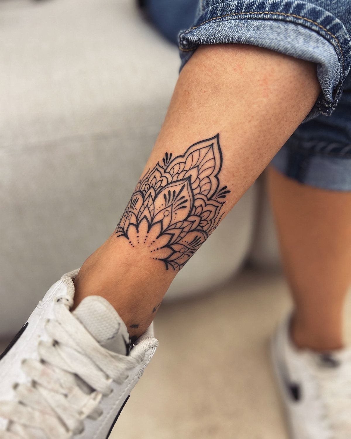 Mandala tattoo on a person's ankle wearing white sneakers and blue jeans.