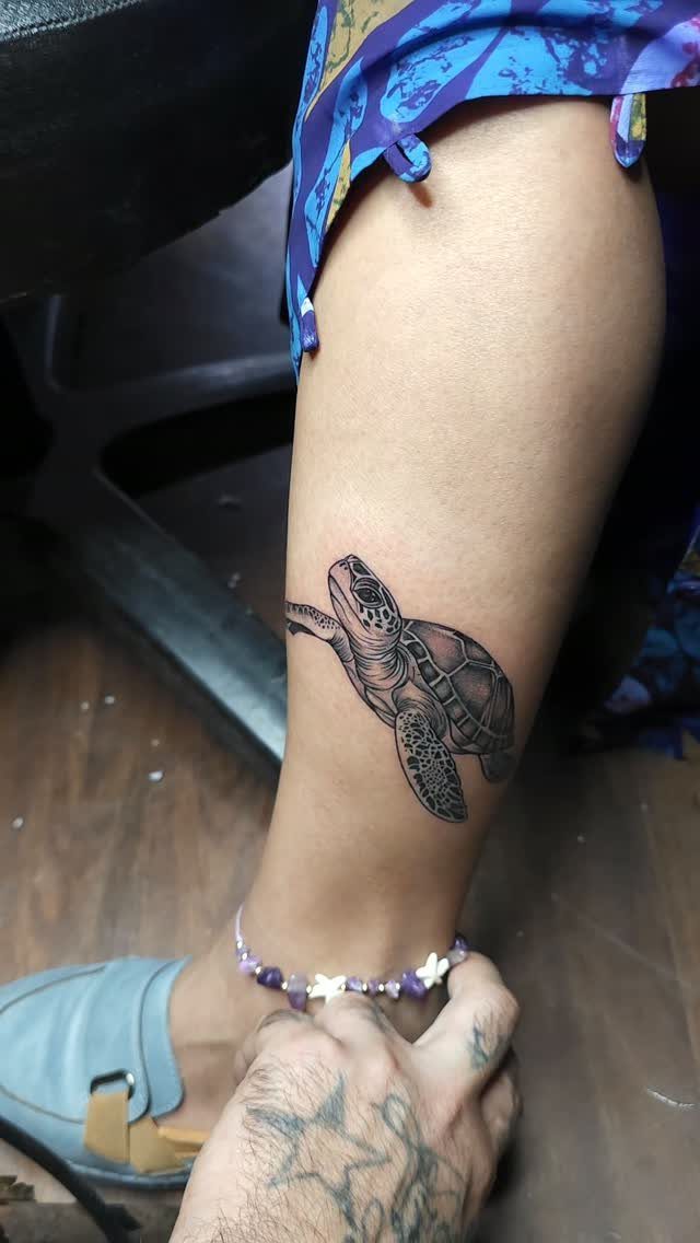 Sea turtle tattoo on a lower leg above the ankle with a beaded anklet.