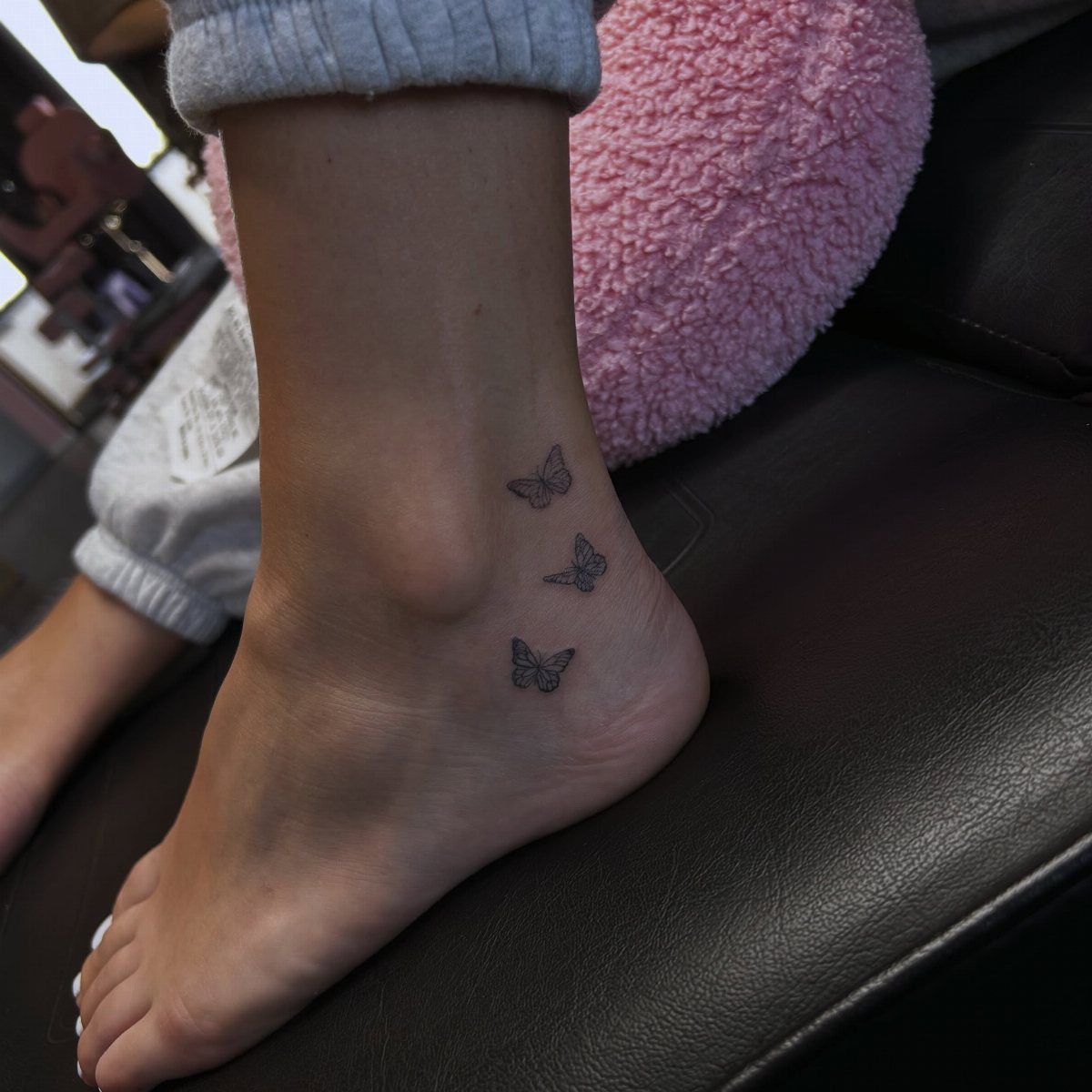Three tiny black butterfly tattoos on a person's ankle and side of foot.