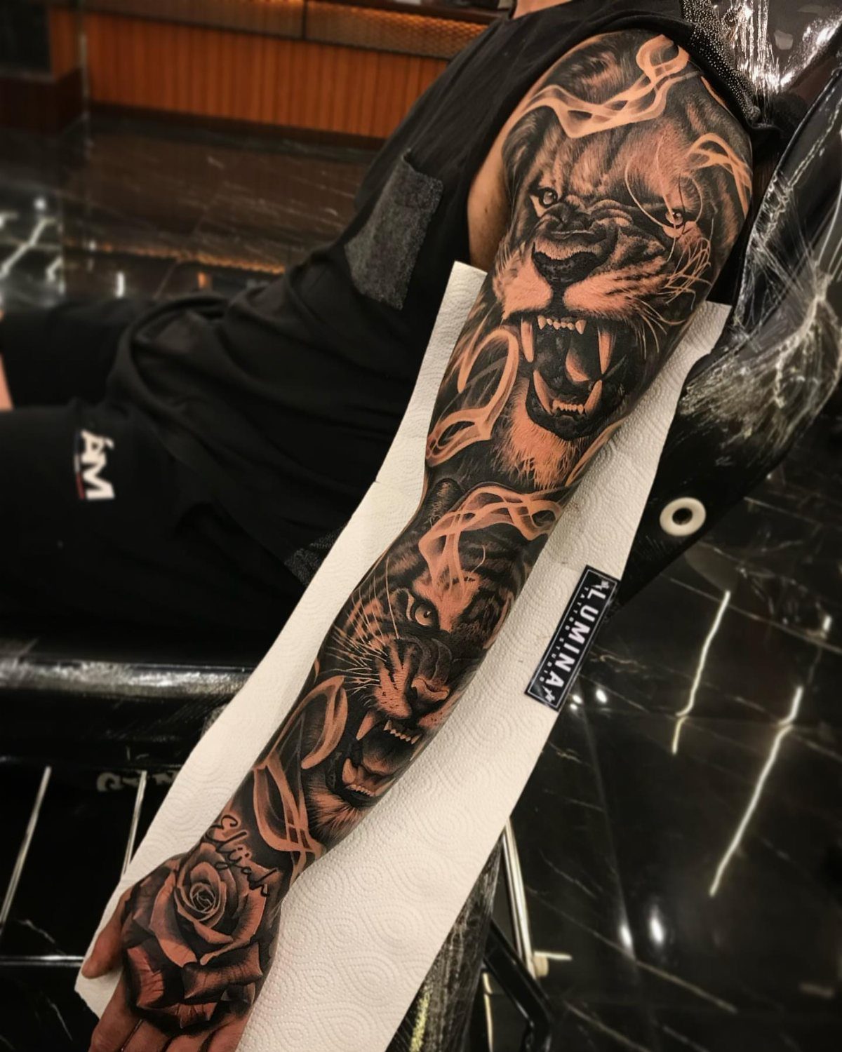 Full sleeve tattoo of roaring lions and a rose on a person's arm.