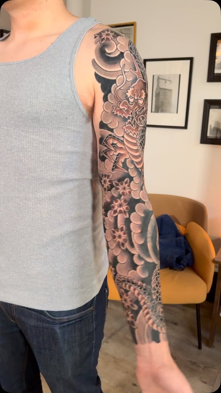 Full arm sleeve tattoo featuring a Japanese dragon, clouds, and floral patterns.