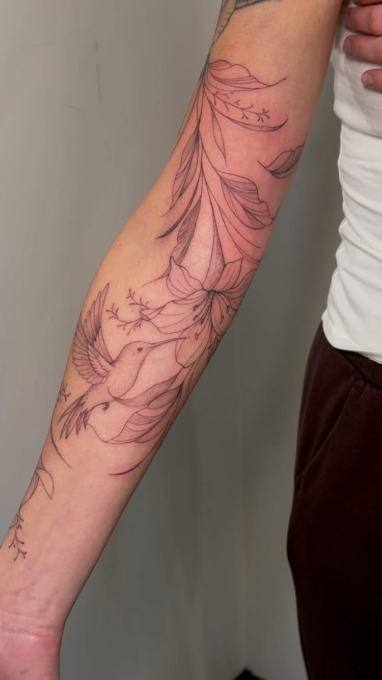 Fine line tattoo of a hummingbird and flowers on a person's arm.