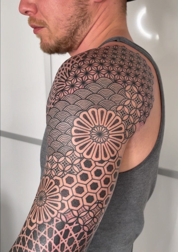 Geometric sleeve tattoo with intricate black patterns on a man's shoulder and arm.