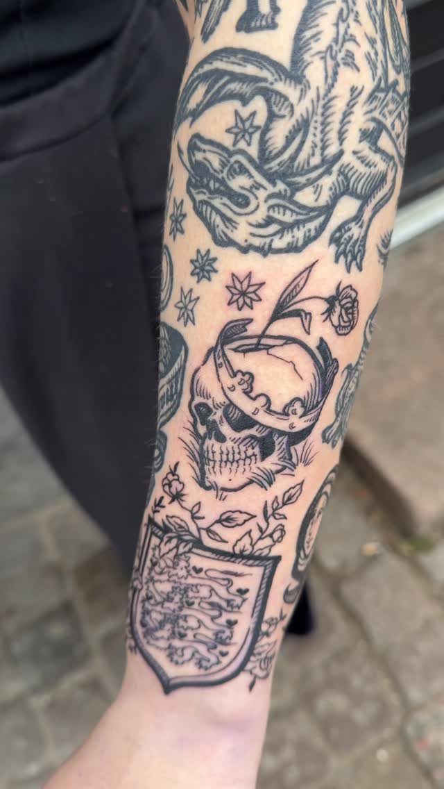 Arm with patchwork sleeve tattoos featuring a dragon, skull, and heraldic shield.