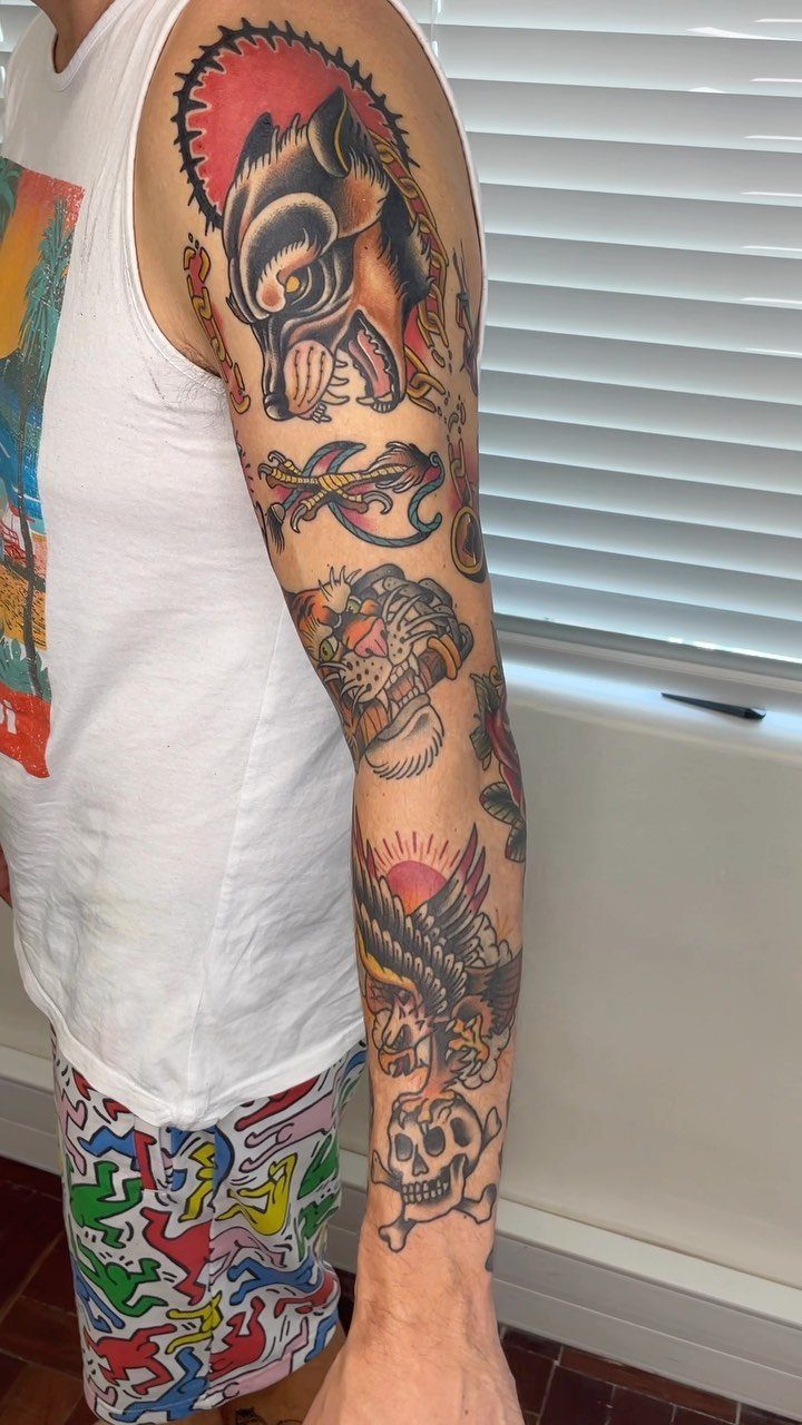 Full arm sleeve tattoo featuring traditional American style wolf, anchor, and skull designs.
