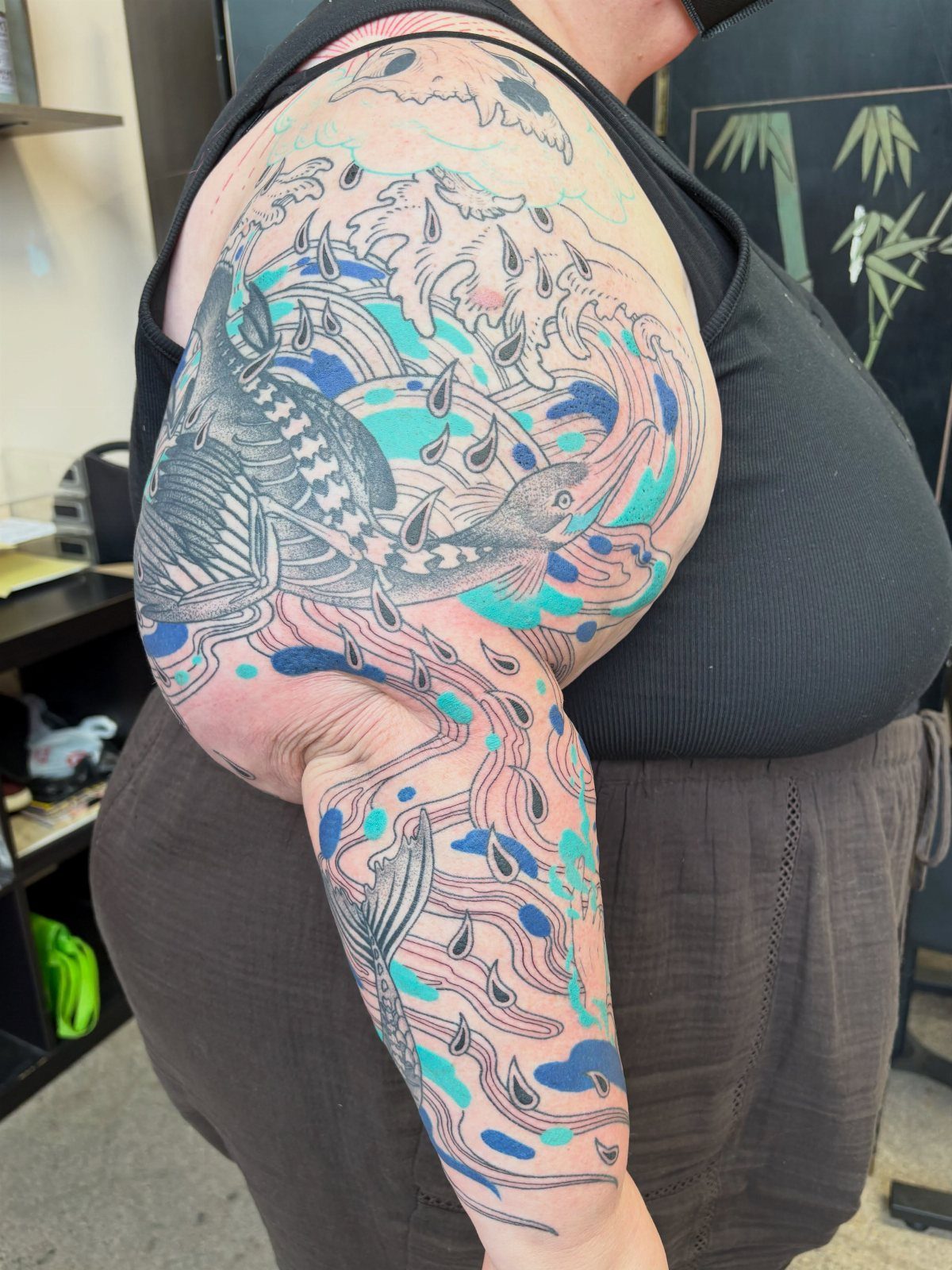 Koi fish sleeve tattoo with blue and teal watercolor splashes on an arm.