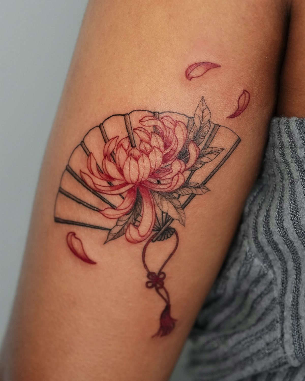 Tattoo of a red chrysanthemum and folding fan on the back of an arm.