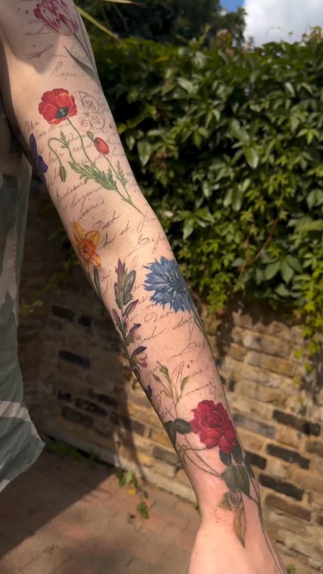 Colorful flower and script tattoos on the back of a person's arm.