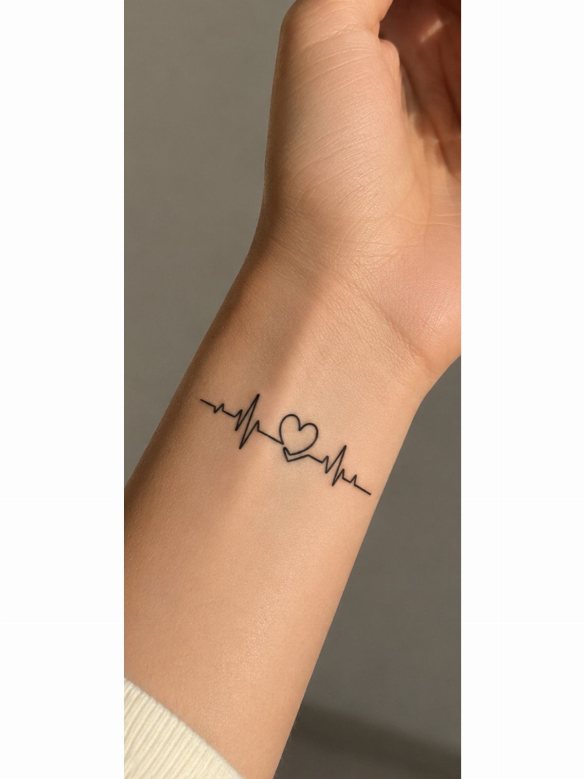Heartbeat line tattoo with a small heart on the back of an arm.