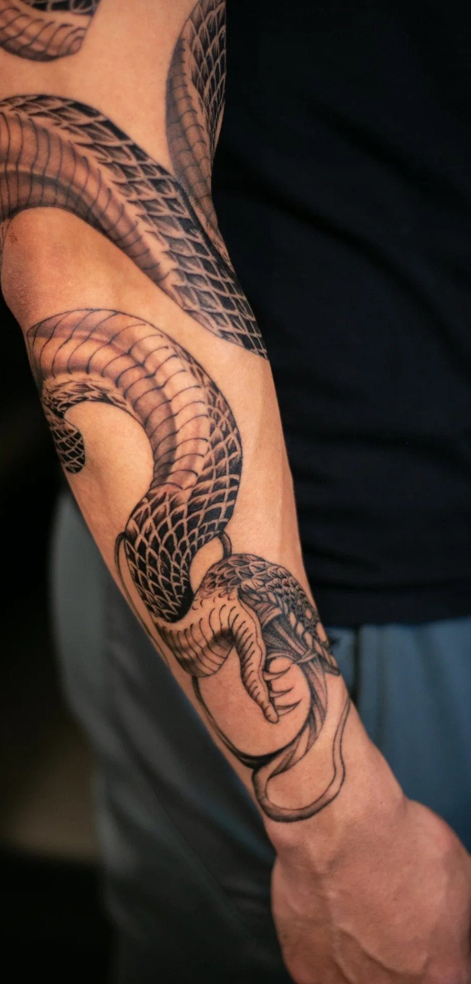 Snake tattoo with detailed scales winding down the back of a person's forearm.
