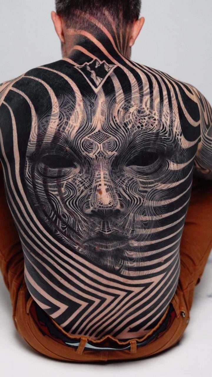 Man's back with a large abstract tattoo featuring a face and bold stripes.