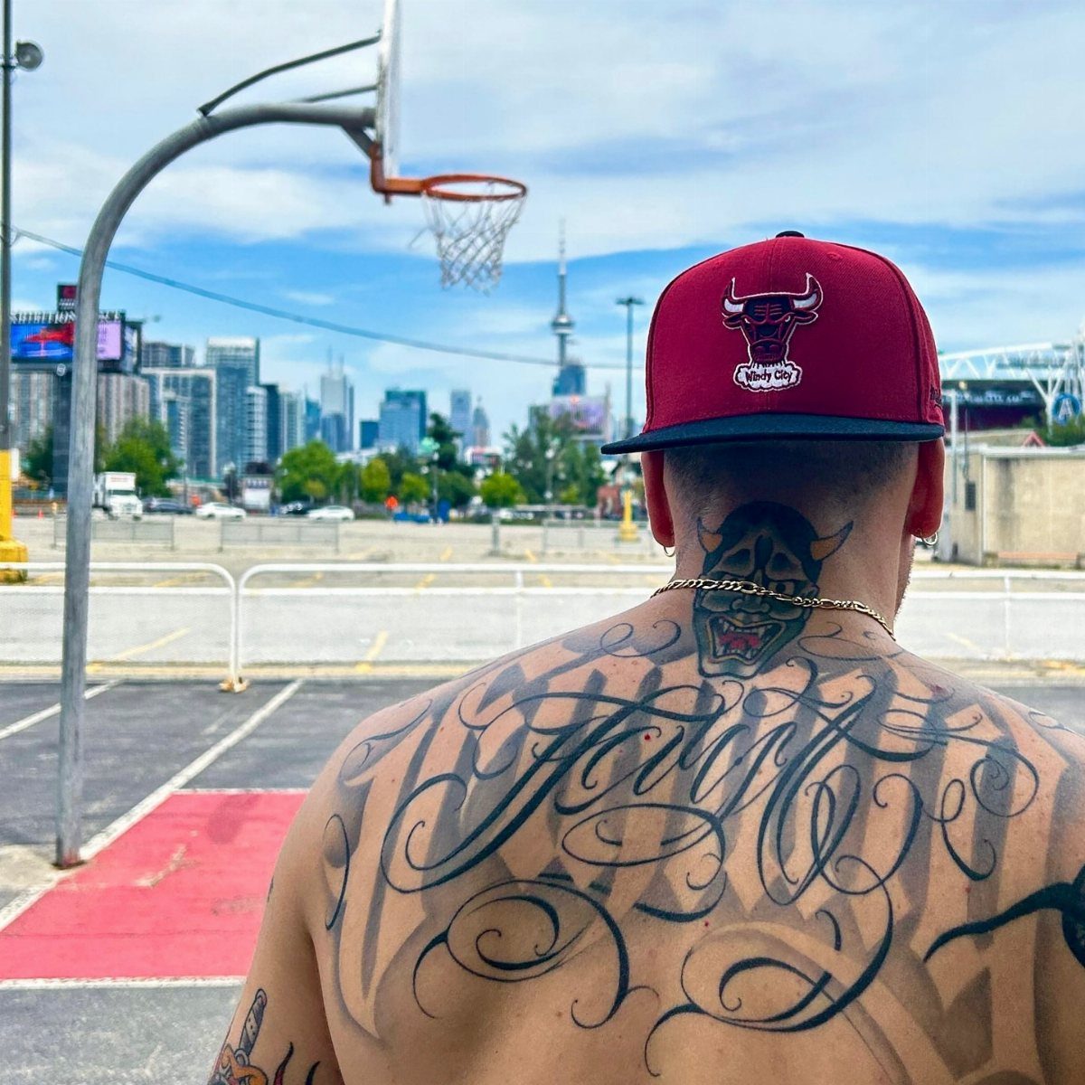 Man with large script and demon tattoos on his back at a basketball court