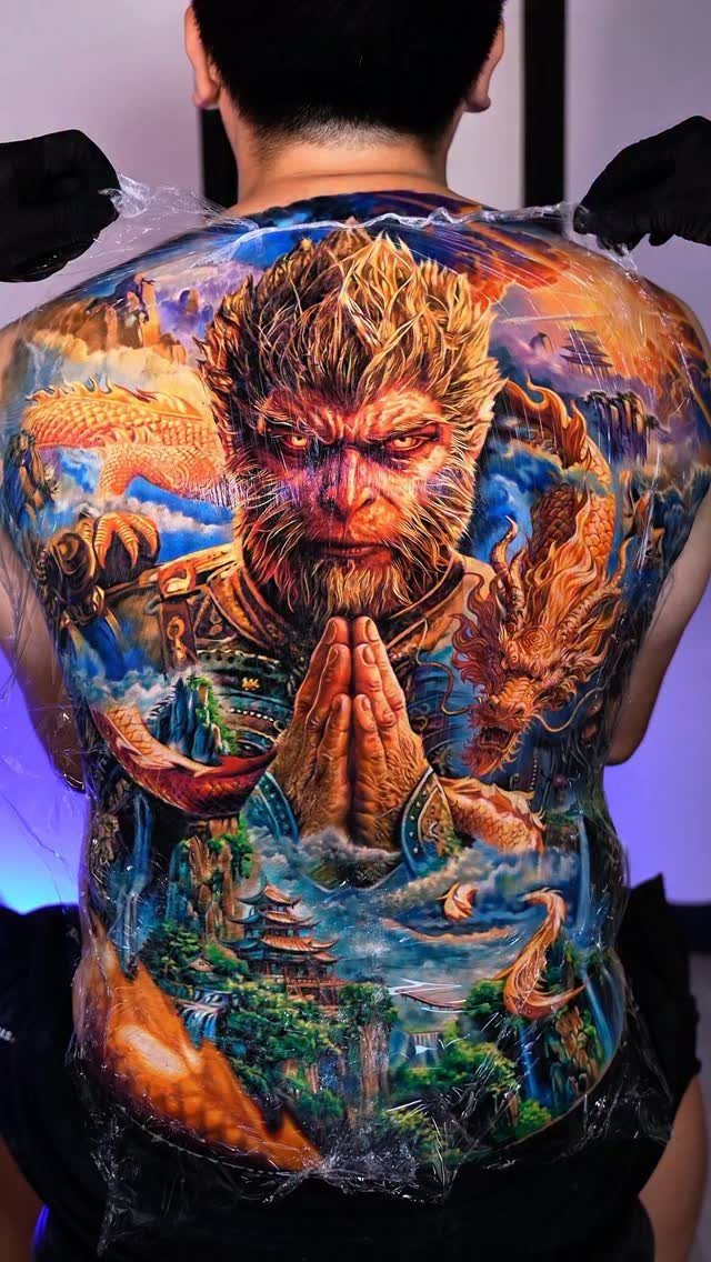 Full back tattoo of a monkey warrior with a dragon and mountain landscape.