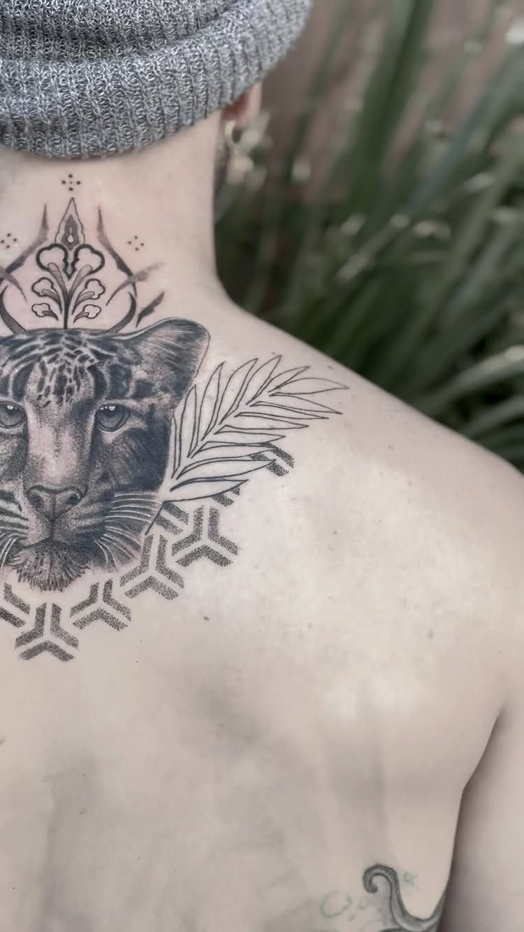 Leopard face tattoo with geometric patterns on a man's upper back and neck.