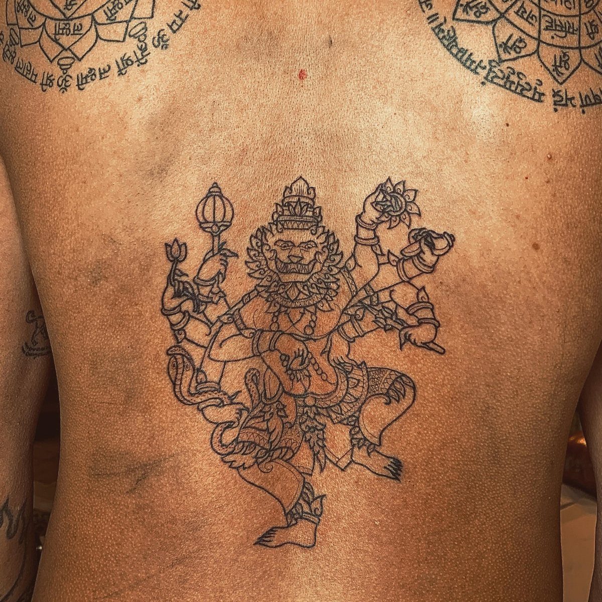 Mythological figure tattoo with multiple arms and lion head on a man's back