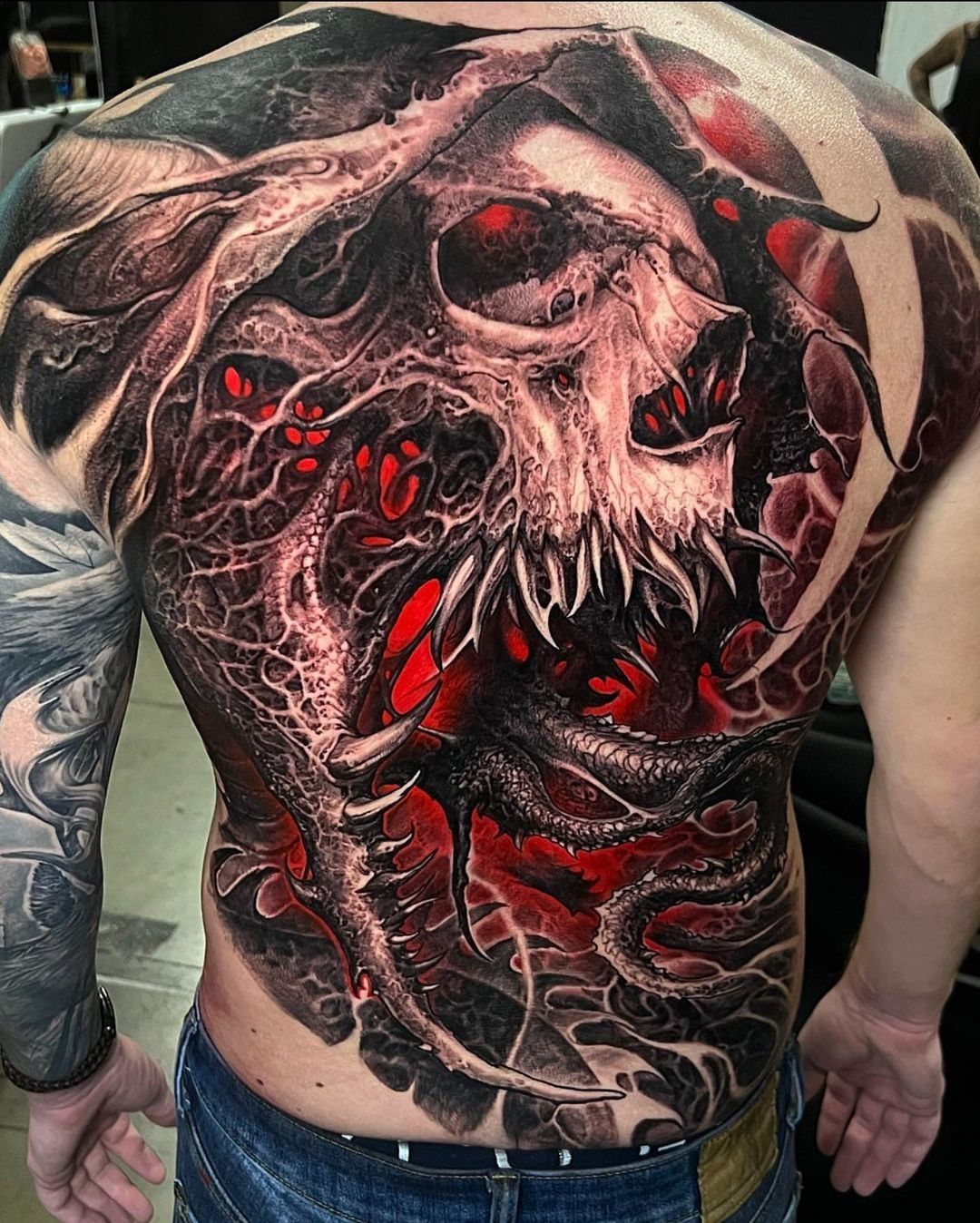 Detailed full back tattoo of a skull with red accents and organic textures.
