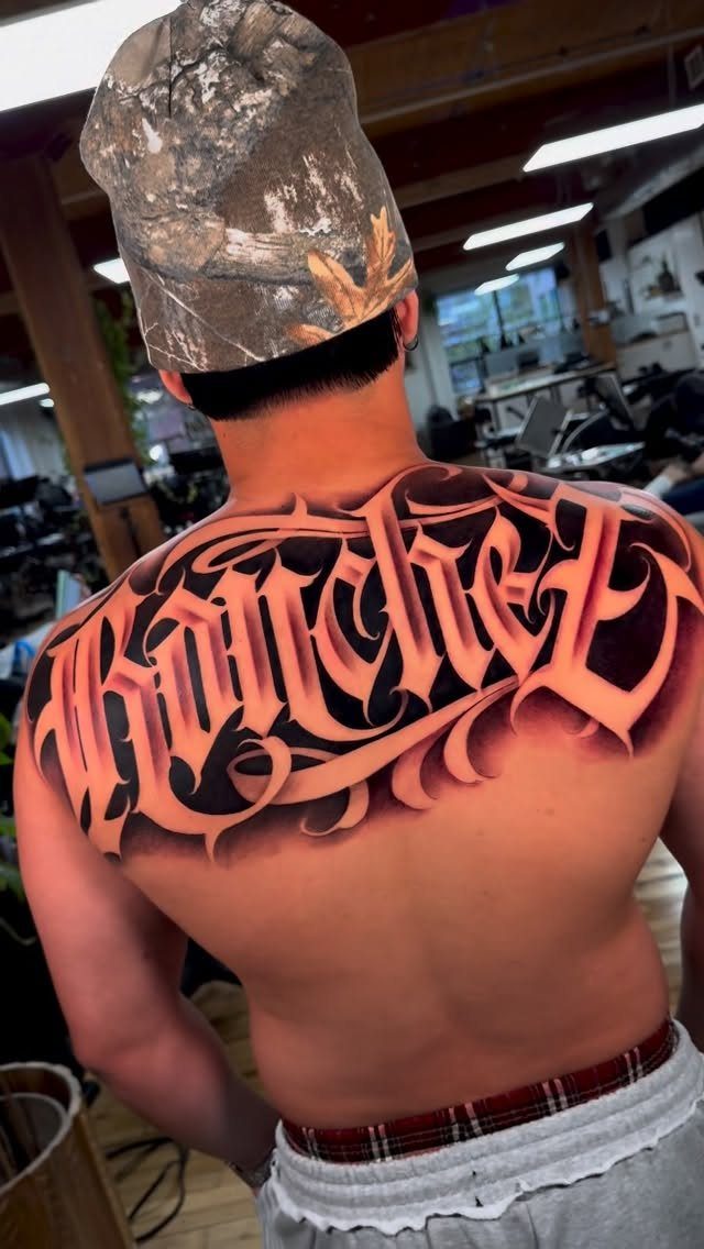 Man with a large stylized script tattoo across his upper back and shoulders.