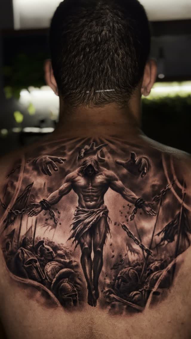 Muscular warrior tattoo on a man's back with chains and fallen soldiers.
