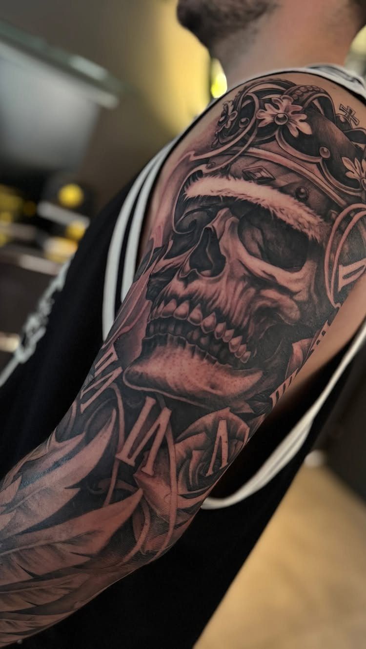 Skull tattoo wearing a crown on a man's upper arm in black and grey.