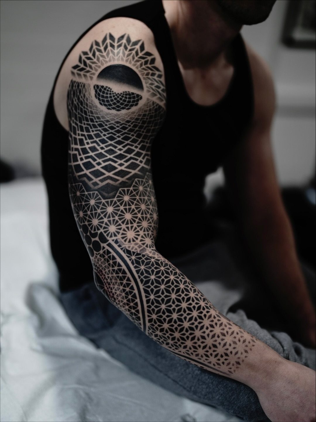 Geometric sleeve tattoo on a man's arm with intricate black ink patterns and shapes.
