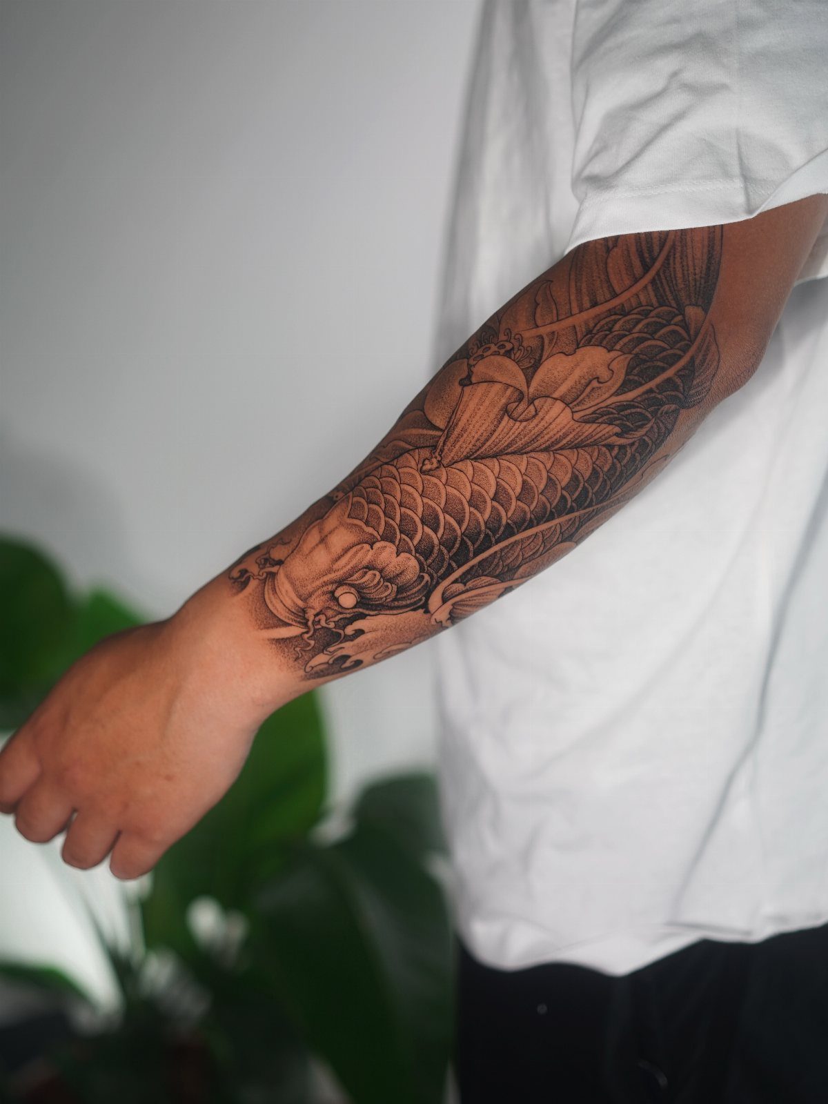 Koi fish and floral tattoo in black and grey ink on a forearm.