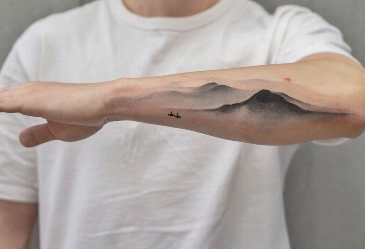 Mountain range tattoo with birds on a person's forearm in black and grey ink