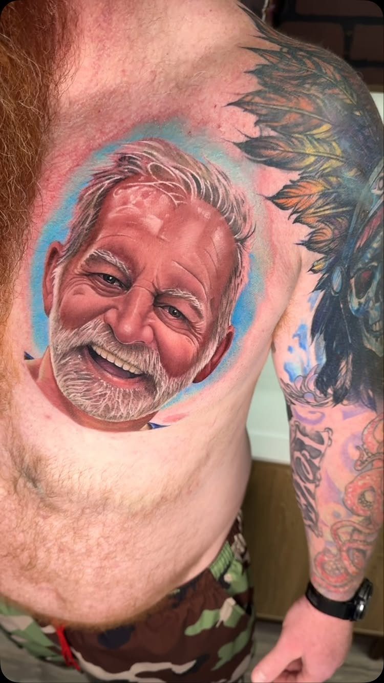 Realistic portrait tattoo of a smiling older man on a person's chest