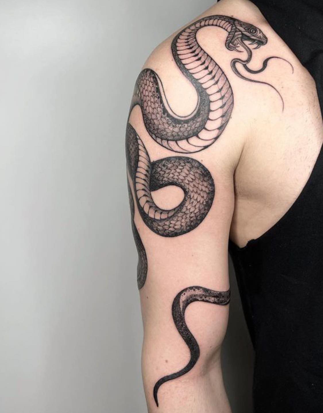 Snake tattoo coiled around a man's shoulder and upper arm in black ink.