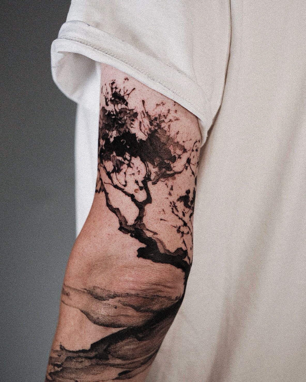 Abstract black ink tattoo of a branching tree on a man's upper arm.