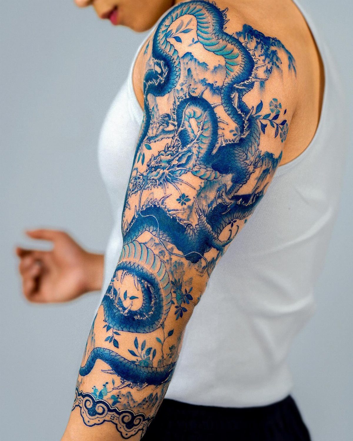 Woman's arm with a detailed blue dragon tattoo from shoulder to forearm.