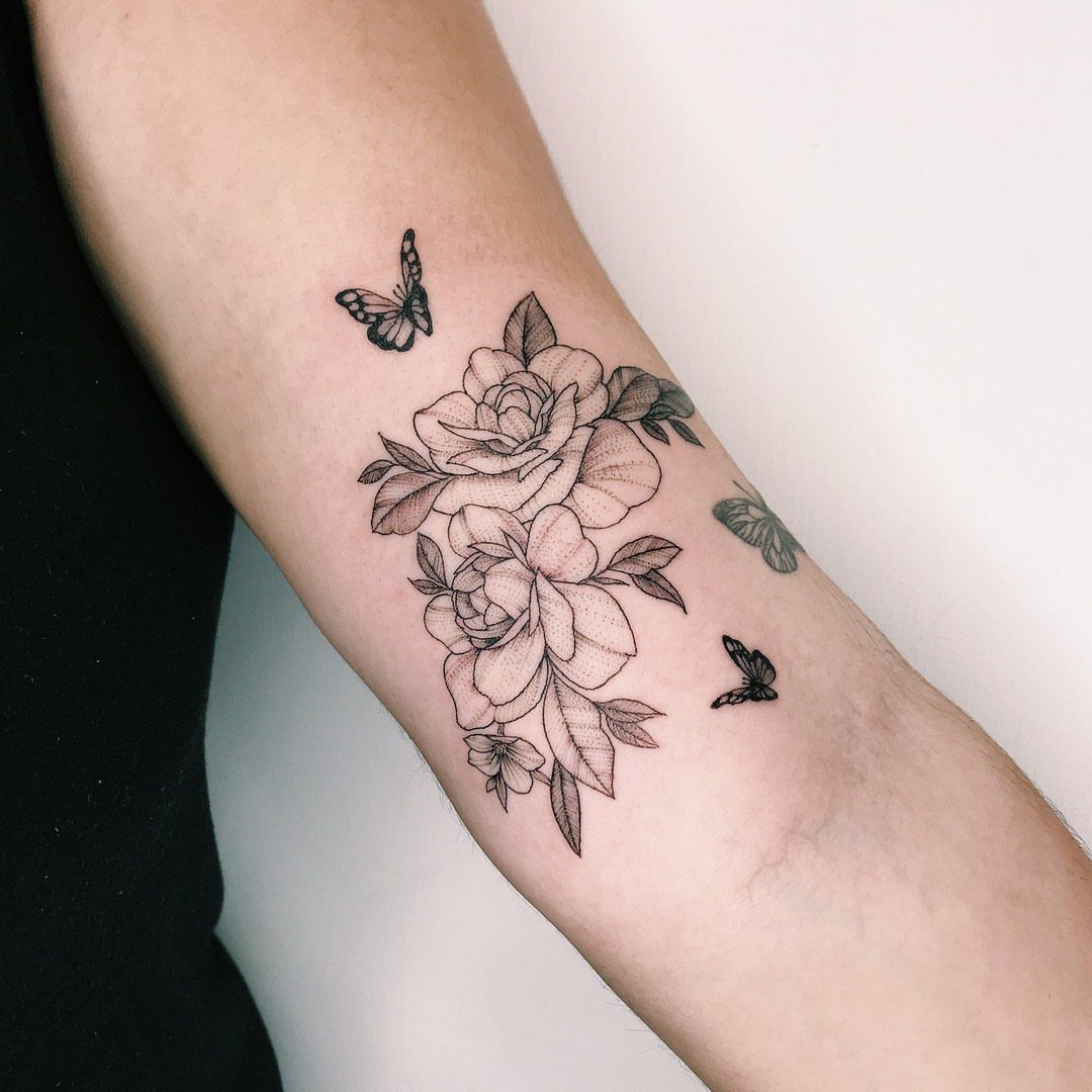 Floral bicep tattoo with roses and butterflies on a person's upper arm.