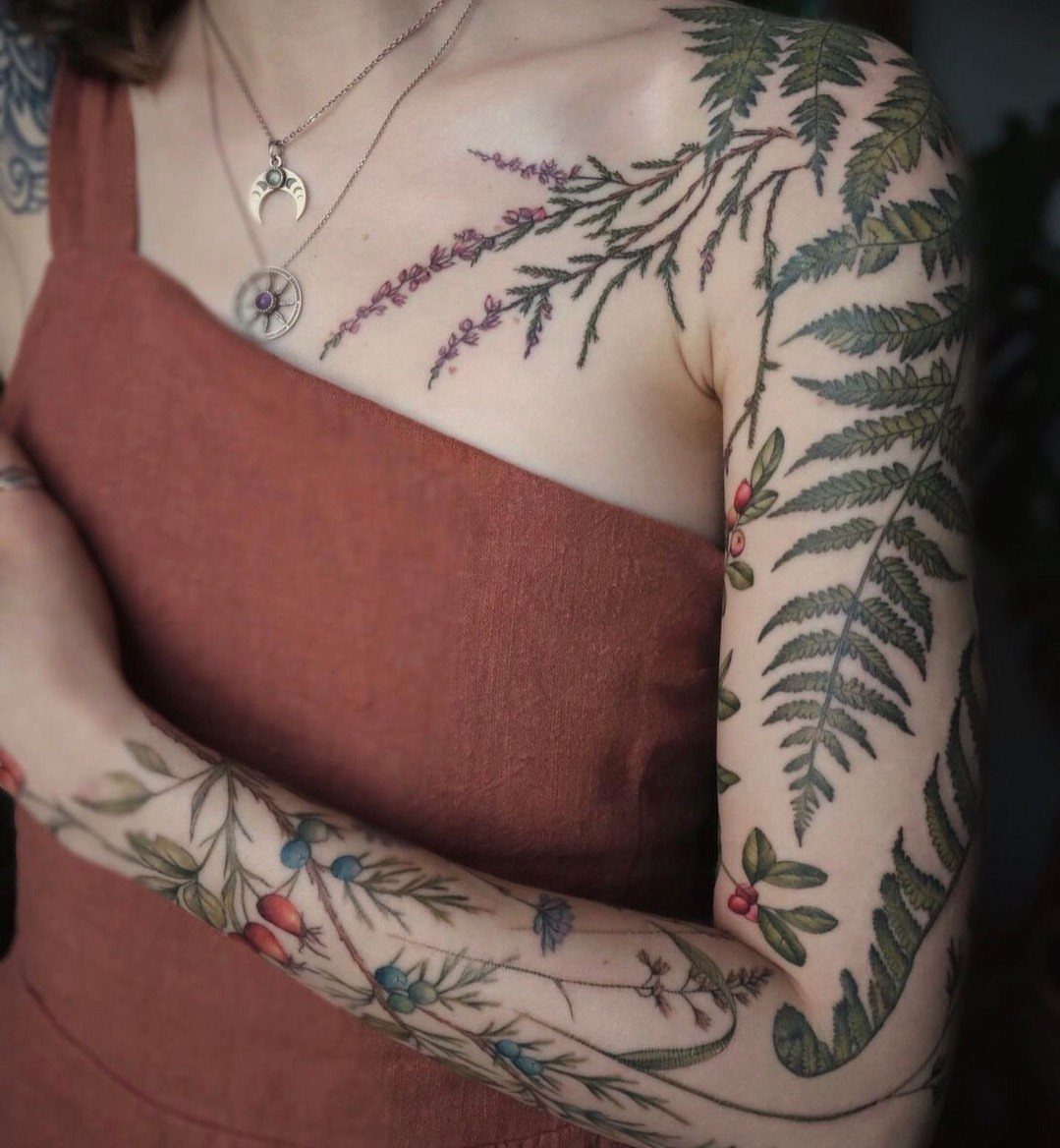 Botanical tattoos of ferns and berries on a woman's bicep and forearm.
