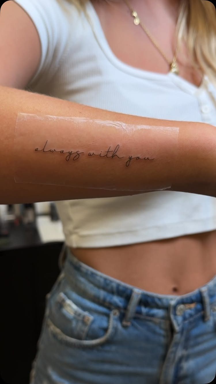 Cursive script tattoo reading 'always with you' on a woman's inner bicep arm.