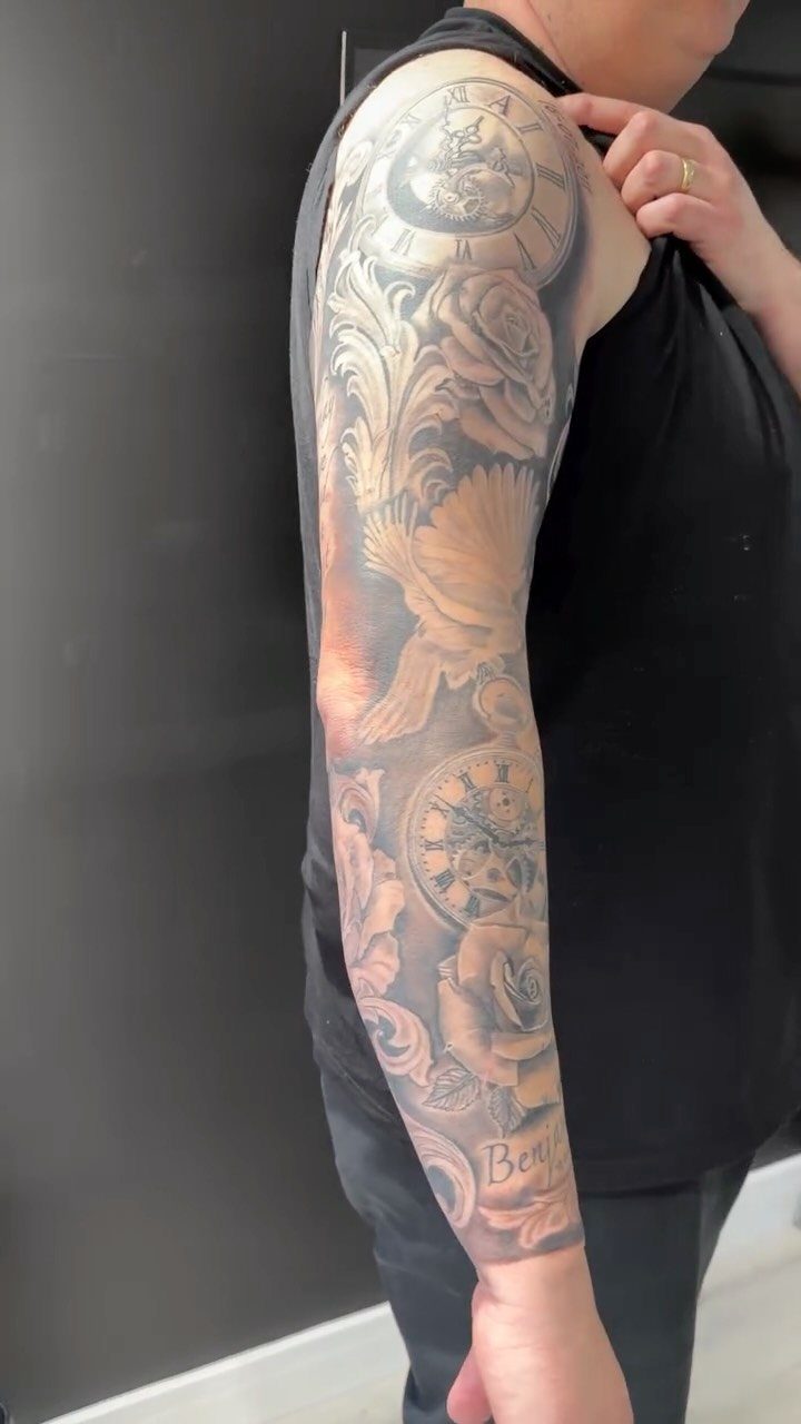 Sleeve tattoo on a man's arm featuring clock faces, roses, and a bird.