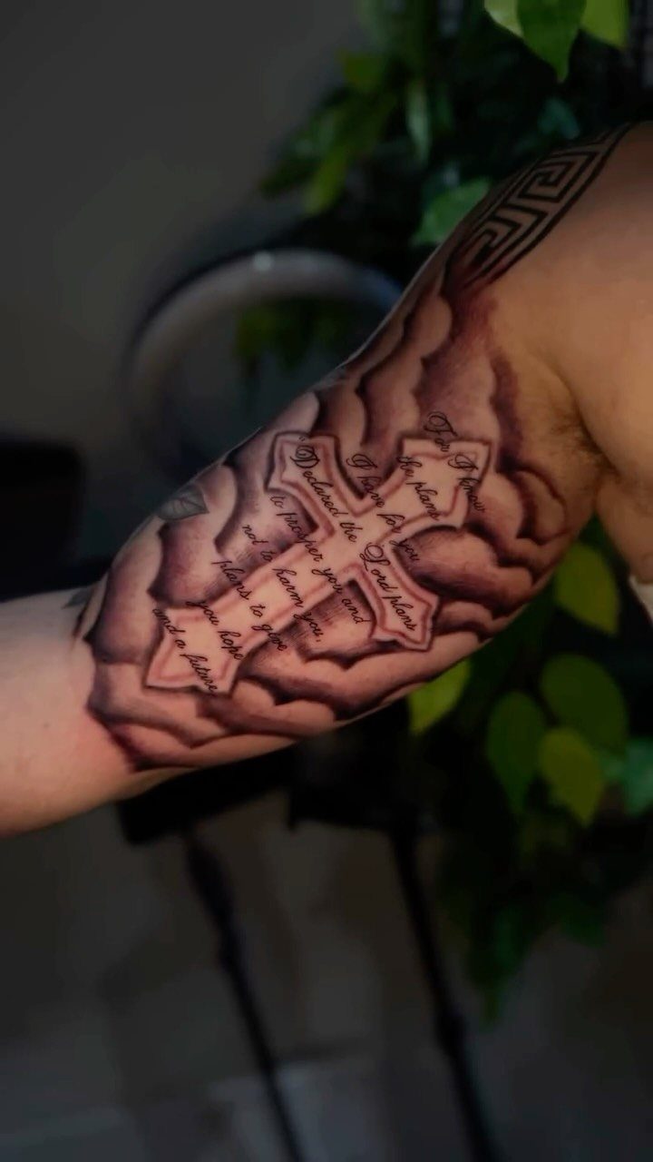 Cross tattoo with script and clouds on a man's bicep and upper arm.