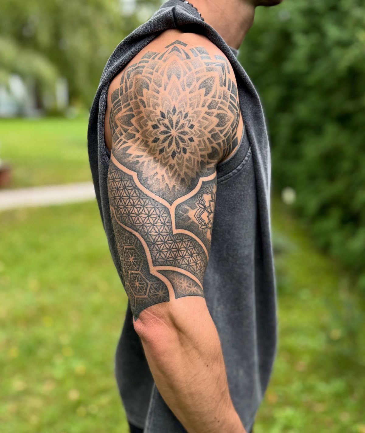 Man's upper arm with a detailed geometric mandala tattoo in black ink