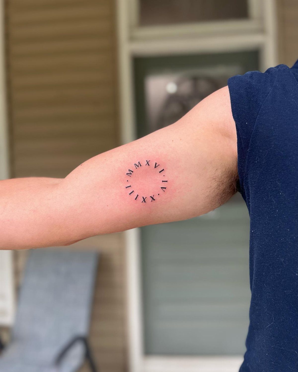 Small circular Roman numeral tattoo on the inner bicep of a man's arm.