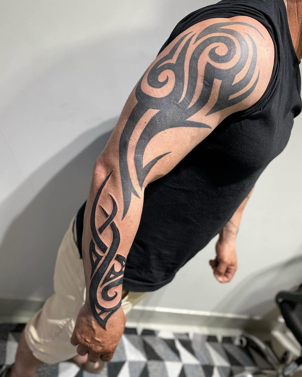 Man's arm with a bold black tribal tattoo from shoulder to forearm.
