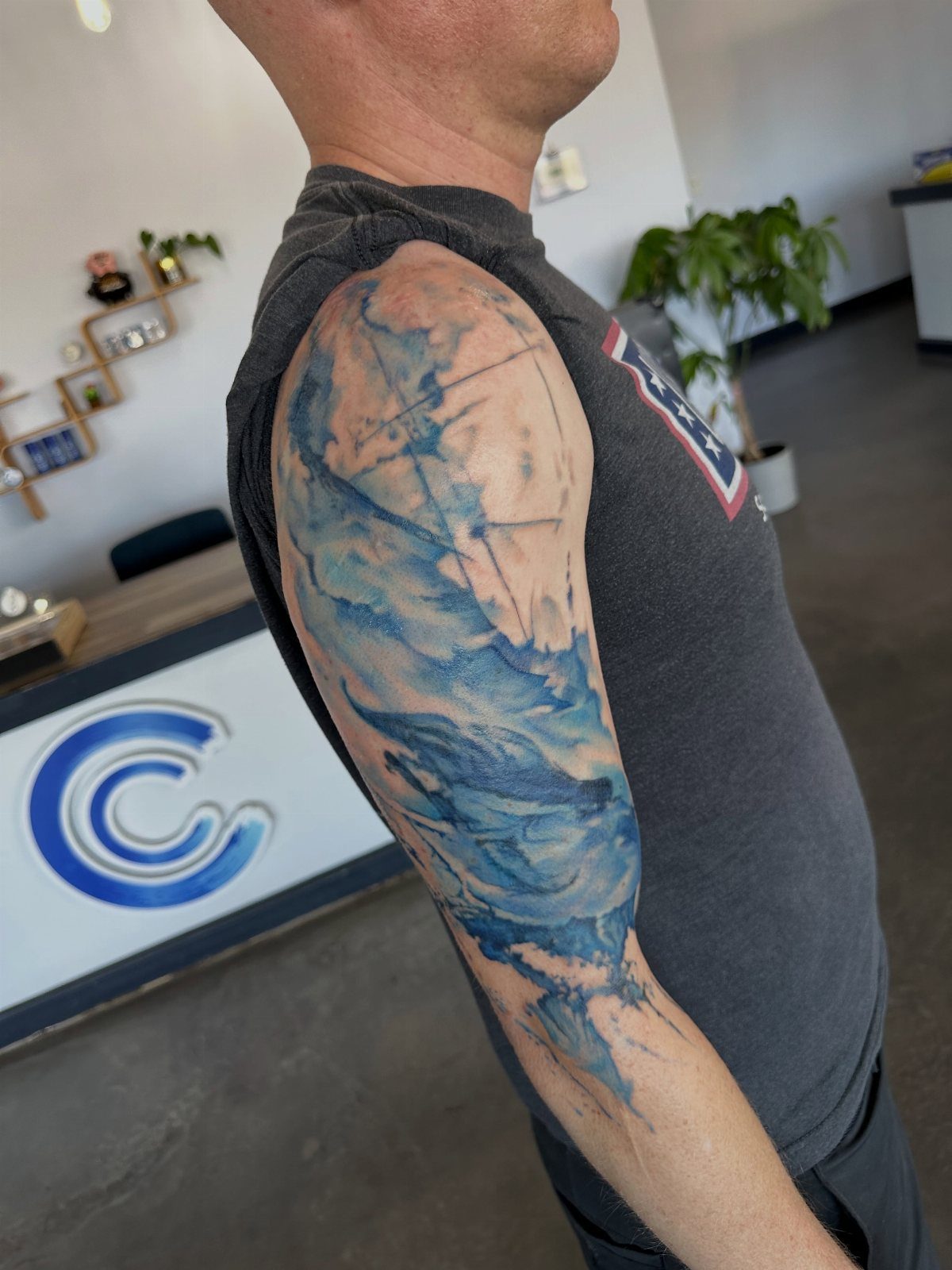 Blue watercolor style tattoo on a man's upper arm and shoulder
