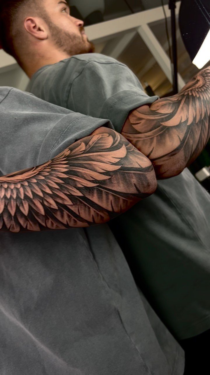 Detailed black and grey wing tattoos covering the biceps of a man.