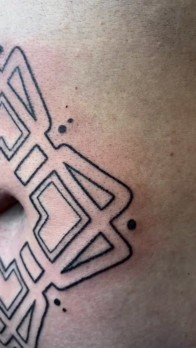 Geometric black ink tattoo with abstract angular lines and dots on fair skin.