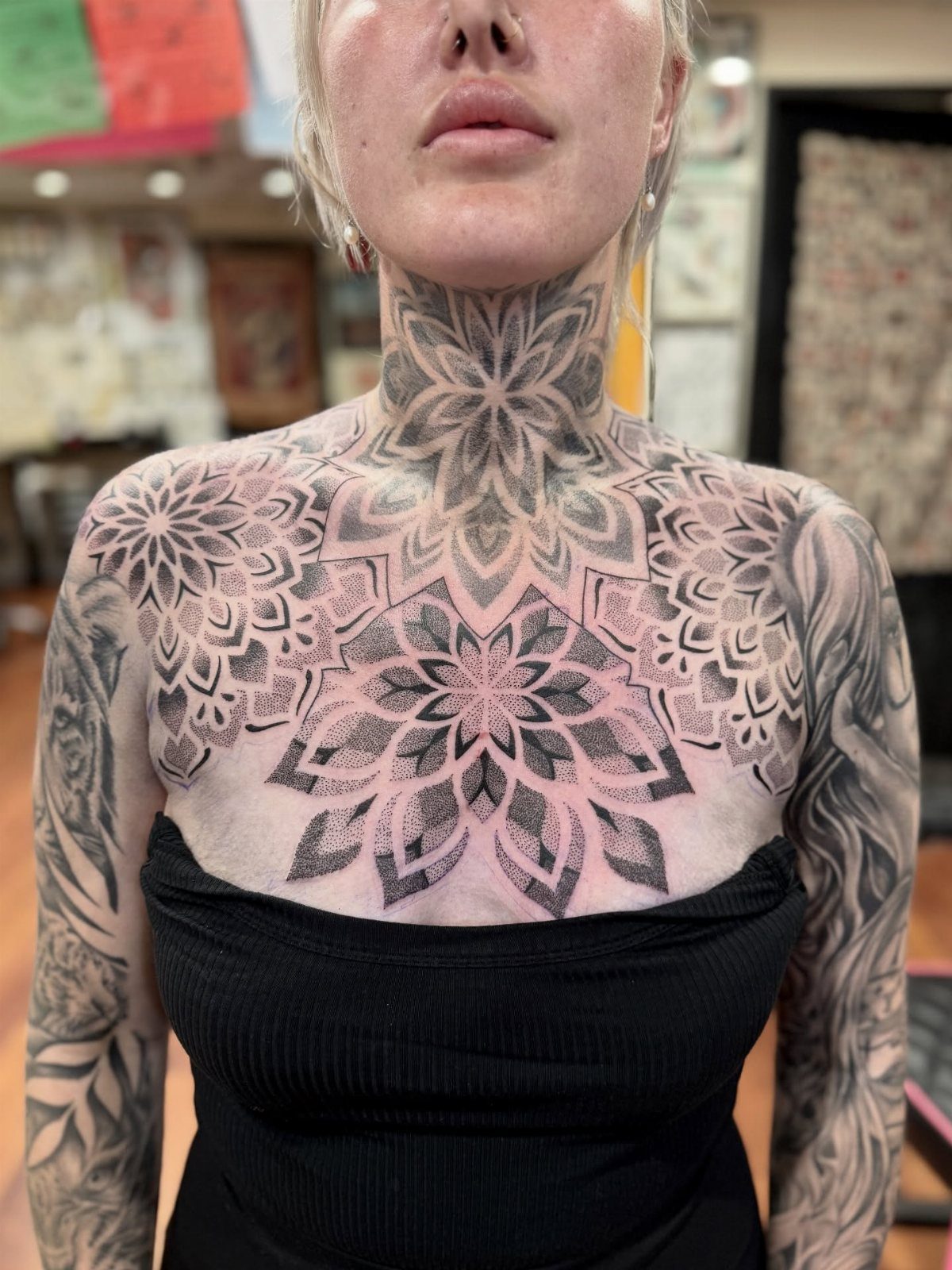 Woman with large, intricate black ink mandala tattoos on her neck and chest.