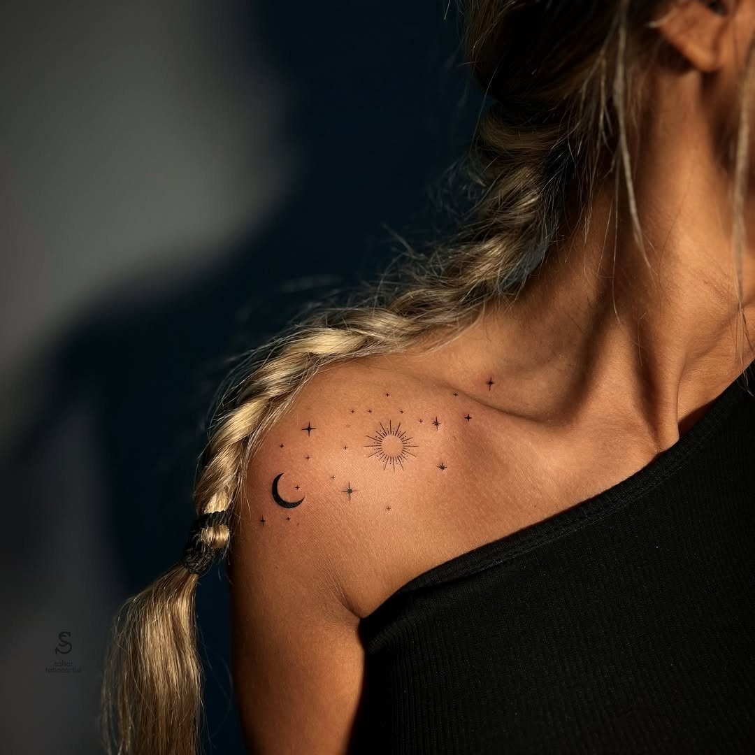 Woman's shoulder with small black tattoos of a crescent moon, sun, and stars.