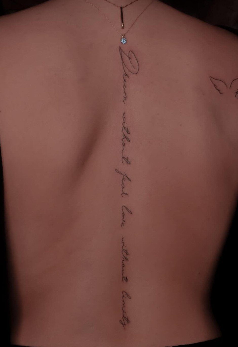 Woman's back with a vertical script tattoo running down the center of her spine.